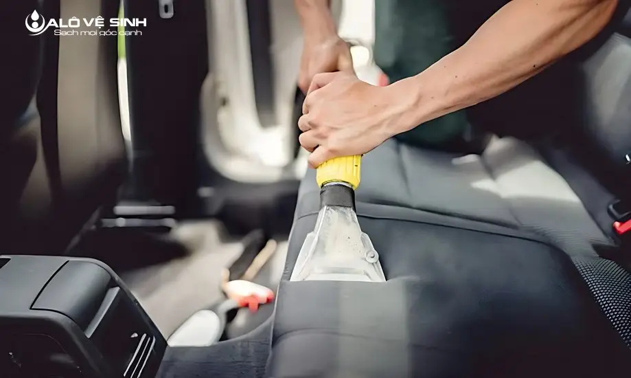 Người đang sử dụng máy hút bụi để làm sạch bụi trên nệm ghế ô tô