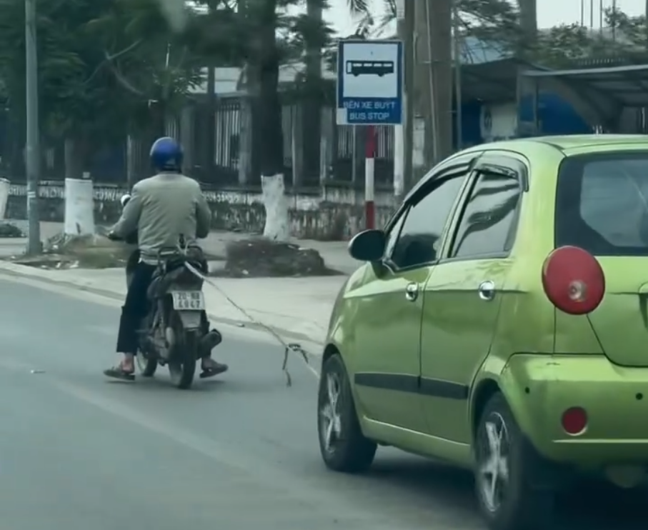 Xe máy kéo ô tô bằng dây thừng trên đường